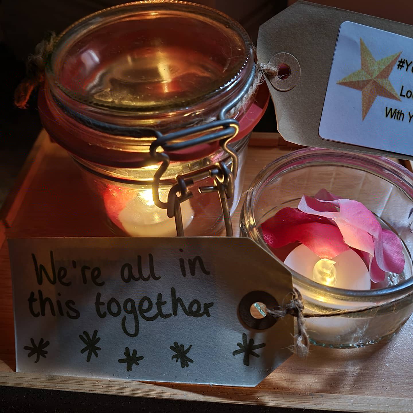 Tea lights in jam jars with faux flower petals with a tag saying 'we're in this together'