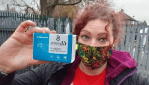 Adult volunteer with a face mask on holding up a oximeter