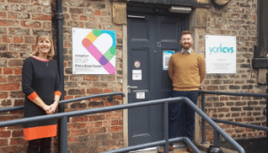 Bev stood to the left and Drew to the right - both smiling at the camera in front of the Priory Street Centre, a historic building in York.