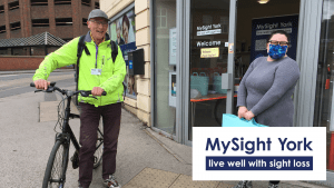 Male stood with a cap and high vos jacket next to a bike and a woman stood with a facemask on outside the MySight York Office.