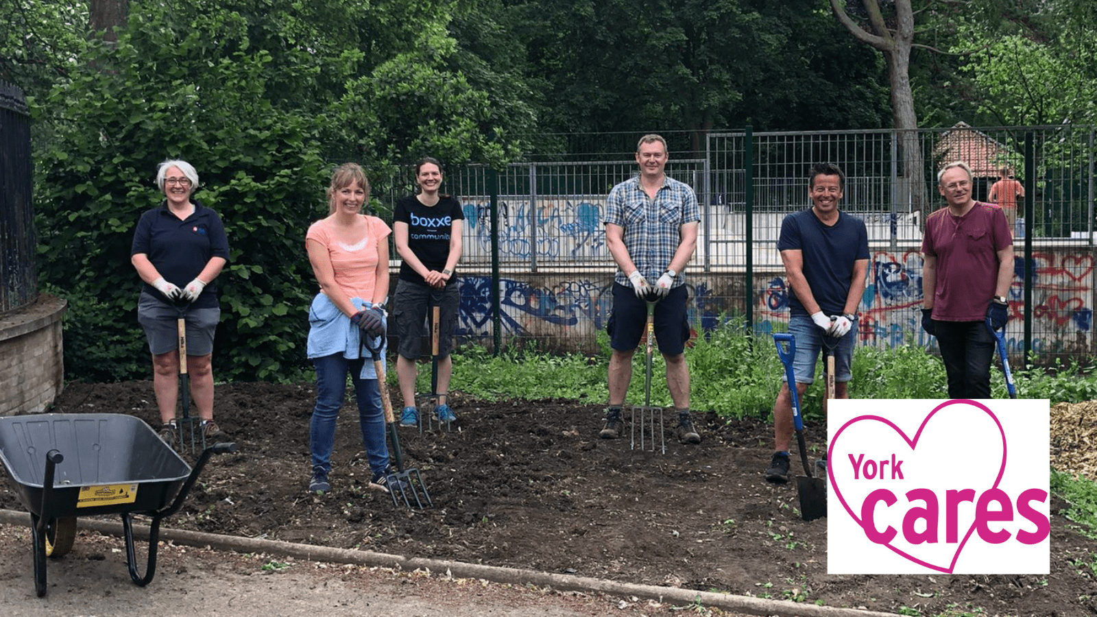 Image of a 6 adults socially distanced in Rowntree Park digging an empty flower bed. There is a wheelbarrow in the foreground.