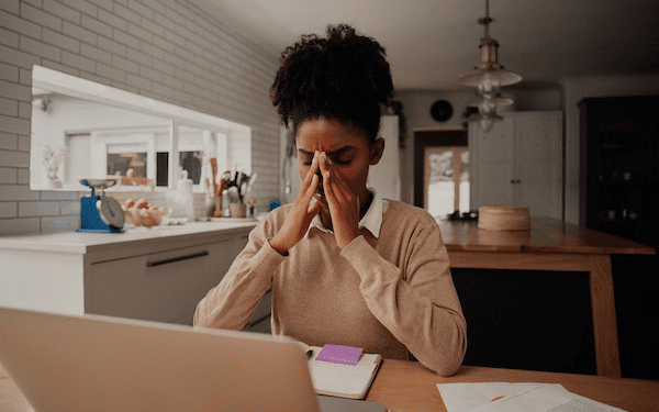 Person sat at laptop for Courtney blog Person sat in front of a laptop and paperwork at a kitchen table. The person is looking worried and has their hands to their face.