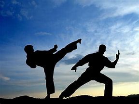 Sam blog martial arts image Silhouette of 2 people practicing martial arts outdoors with a backdrop of blue sky and sun beginning to rise.