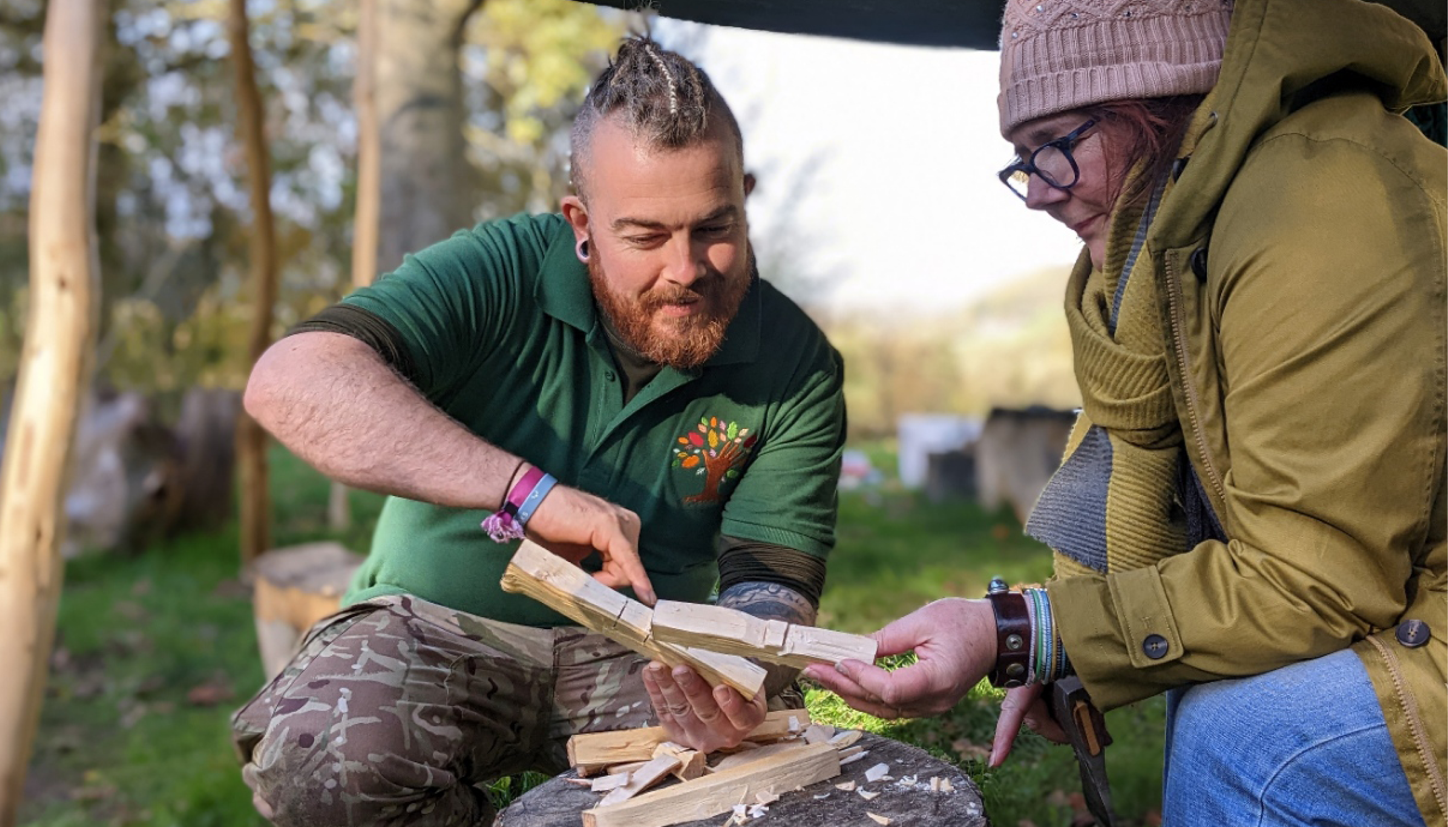 Green Social Prescribing Image shows two people sat outdoors looking a some crafted pieces of art made from wood.