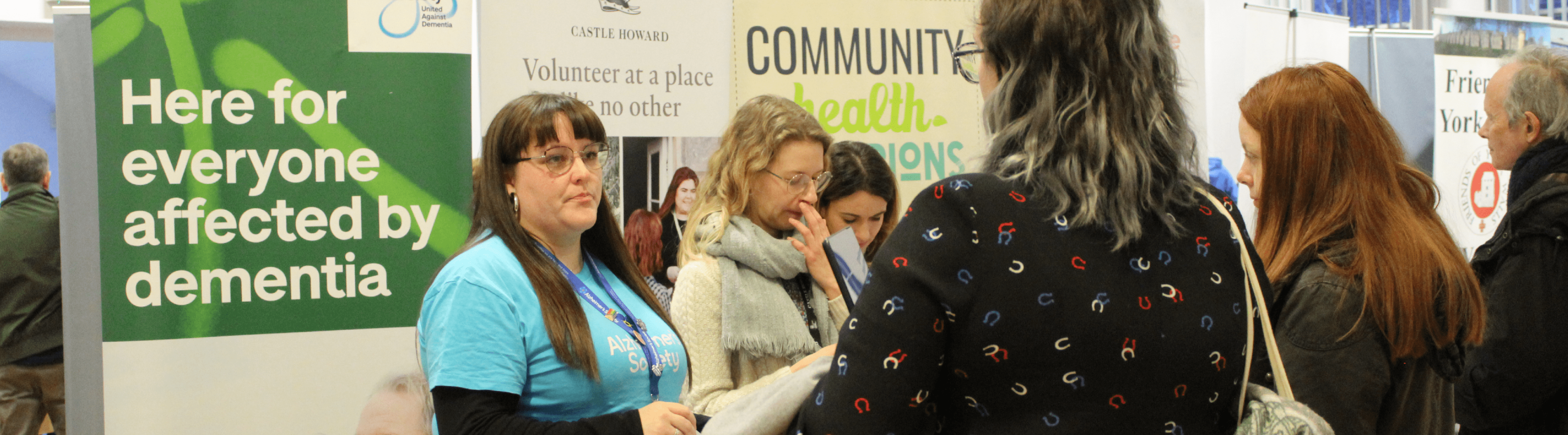 Volunteering Image shows people attending the Volunteer Fair held in 2024. There are pull up banners and people talking to one another.