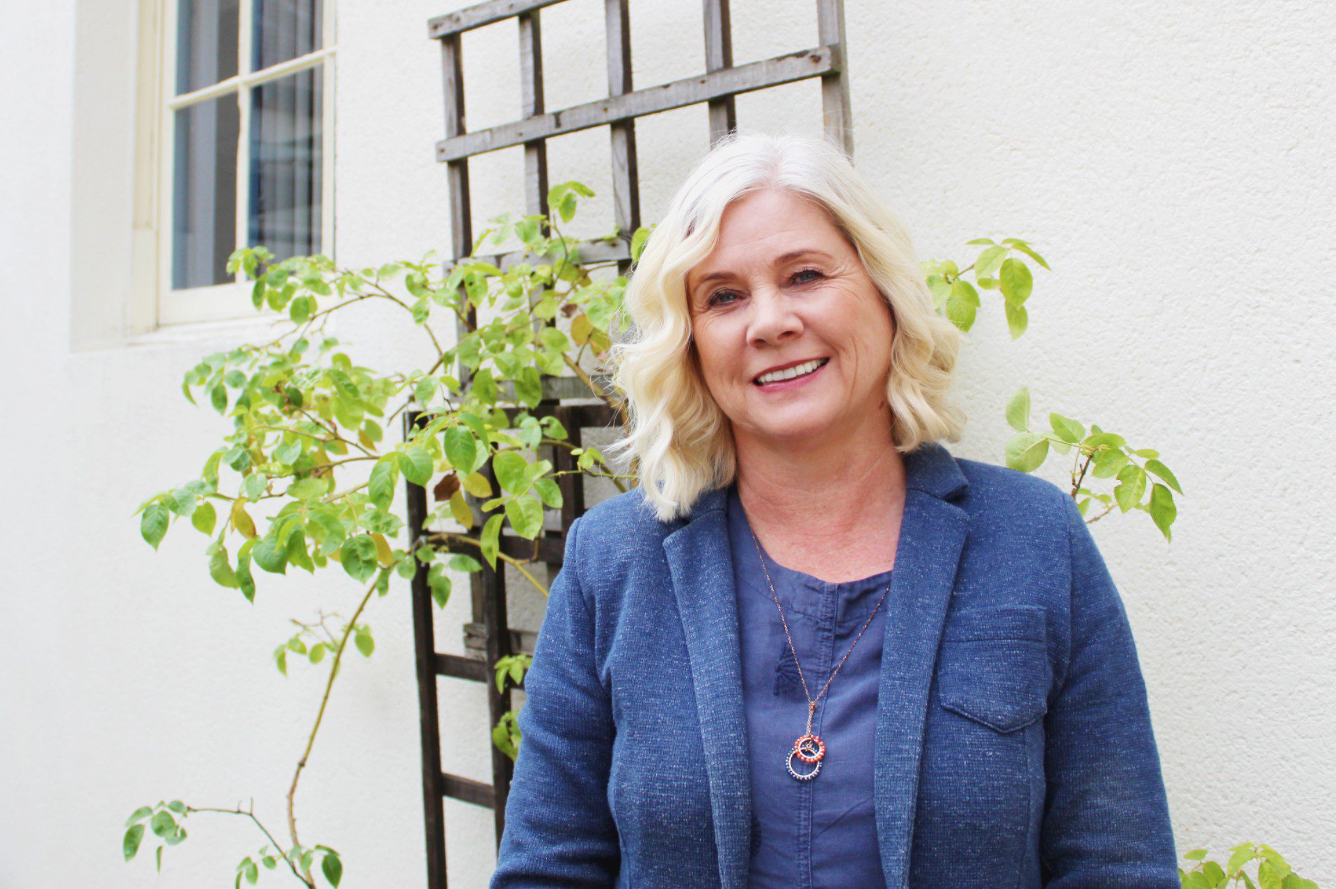 AS - Courtyard Image of a white woman with short wavy blonde hair stood in a courtyard surrounded by plants