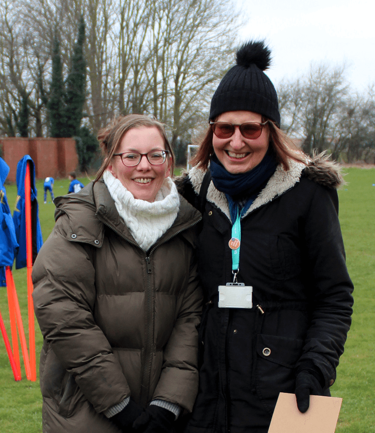 Anne-Marie Carradice and Jane Granville Image shows two women similing at the camera. They are at a under 9's football training session and you can see the football pitch behind them.