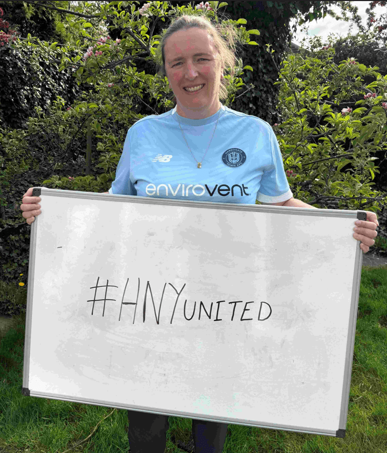 Harrogate_Town A football player from Harrogate Town hold a white board with the words Hashtag H N Y United