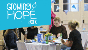 Image of young people sat down at a table. Growing Hope York Logo