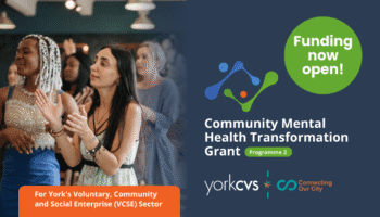 Group of diverse people clapping and engaging in a community event focused on mental health transformation funding in York.
