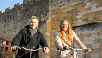 Image of Rhiannon Letman-Wade, Active Travel Commissioner for York and North Yorkshire, and David Skaith, Mayor of York and North Yorkshire on bicycles on a cold but sunny day next to York city bar walls.