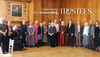 Image shows a group of Trustees at a celebratory event held at the Grand, York. the room has wooden panelled walls and parque flooring.
