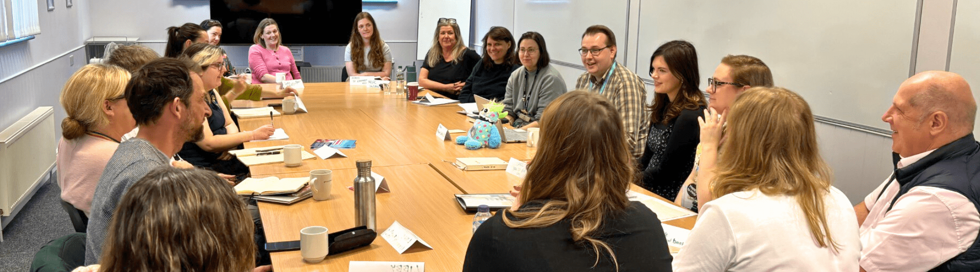 Image of group of people sat round a large meeting room table talking 