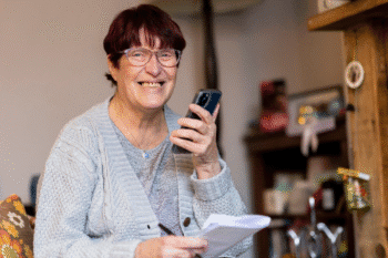 An older woman with brown hair and wearing glasses smiling and talking into a mobile phone