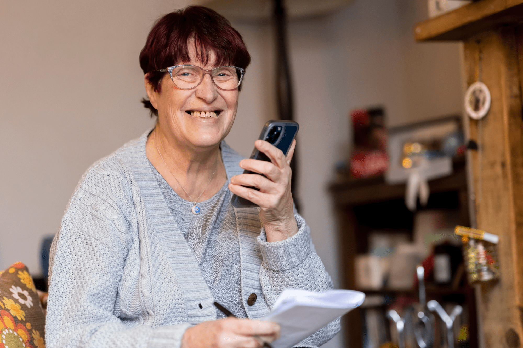 An older woman with brown hair and wearing glasses smiling and talking into a mobile phone