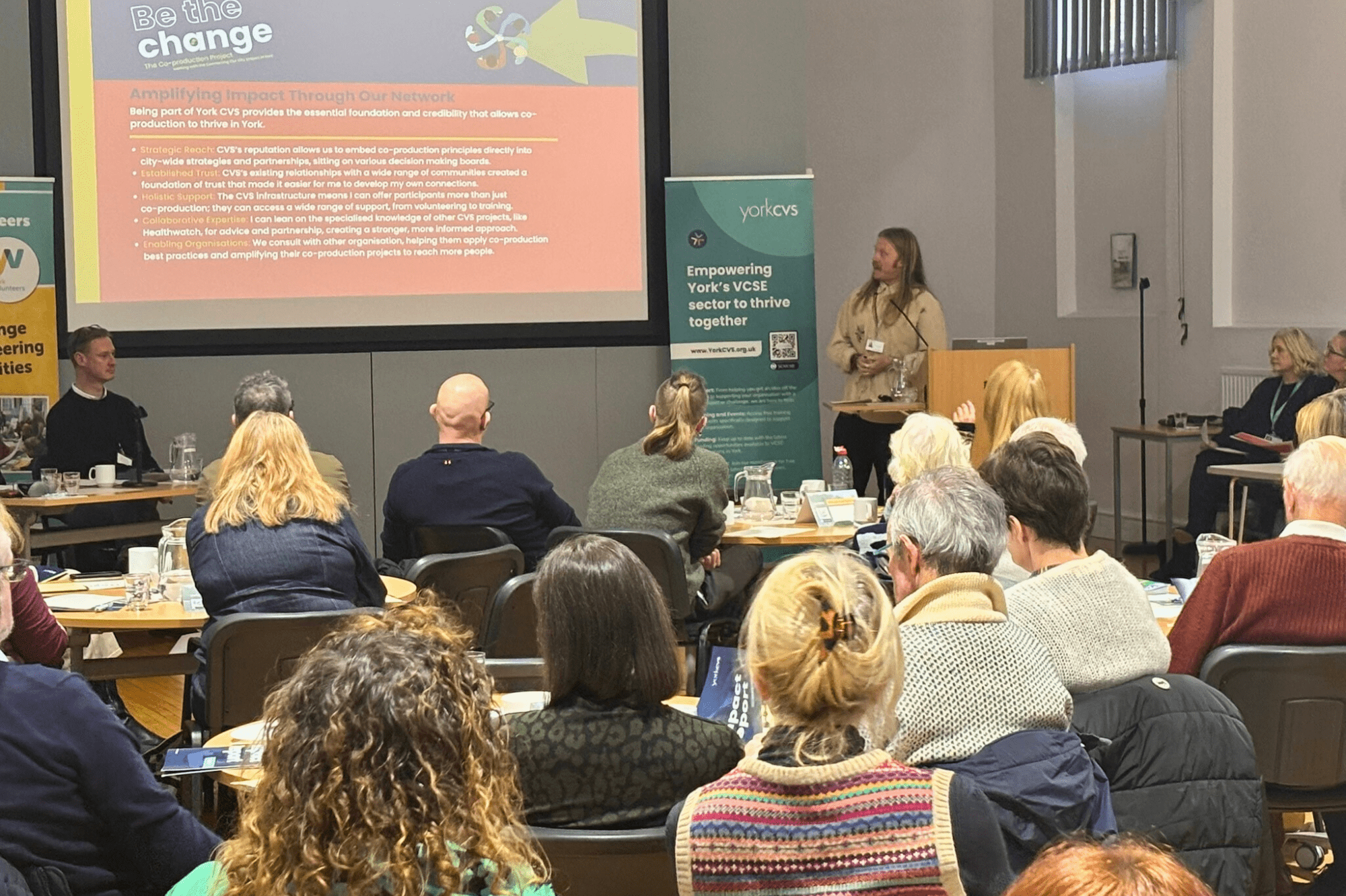 Image of a room full of people sat down watching a presentation
