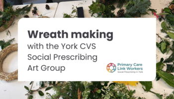 A table covered in natural foliage, pinecones, and wreath-making supplies. Partially made wreaths and green branches are visible. Overlaid text reads: “Wreath making with the York CVS Social Prescribing Art Group” alongside the Primary Care Link Workers logo.