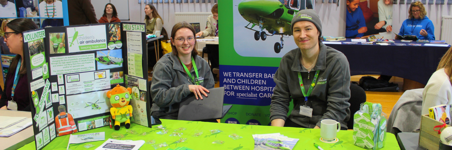 Two people sat down at a stall which is full of leaflets and information 